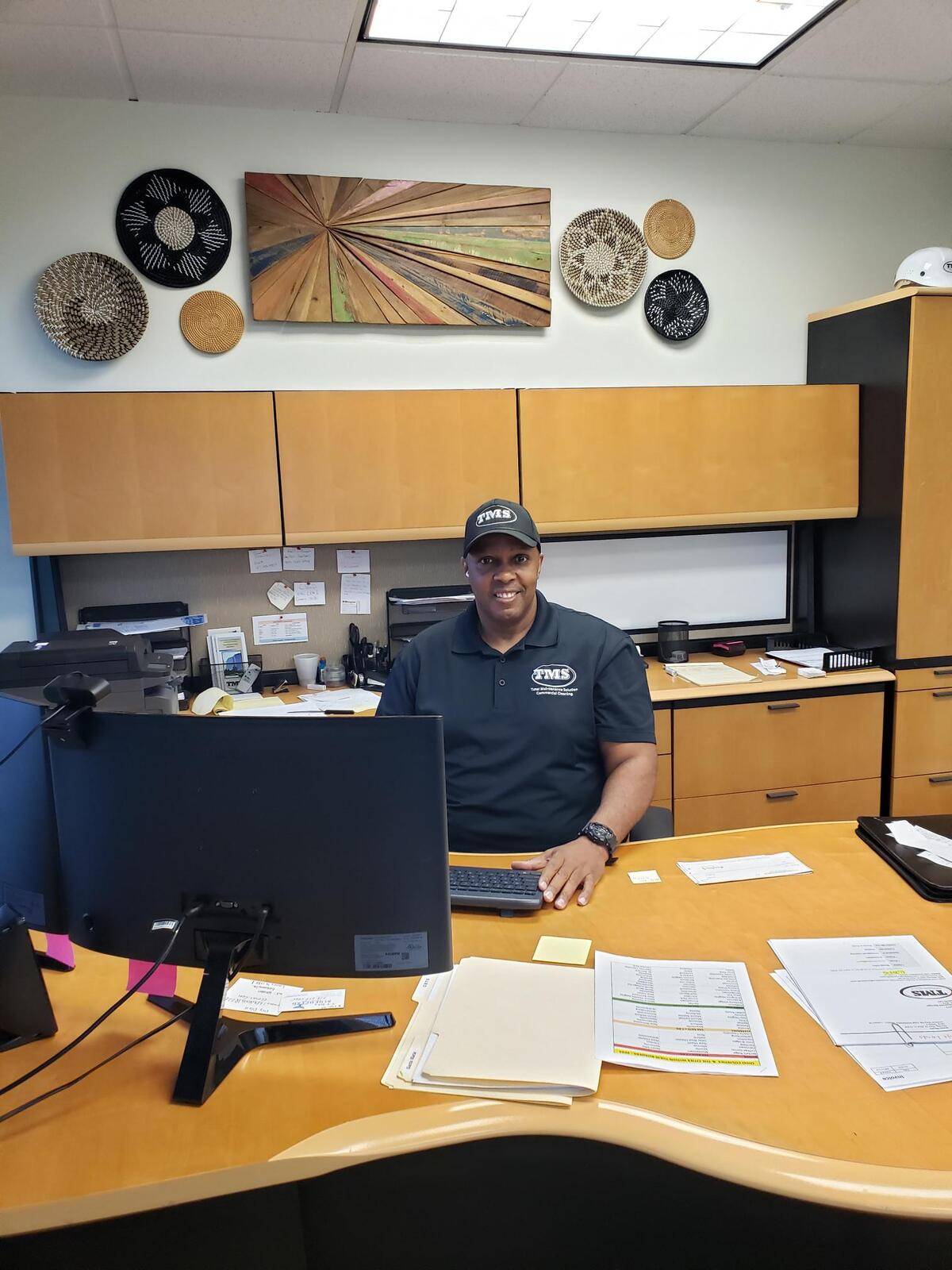 a man smiling while he sits at a desk working on a computer